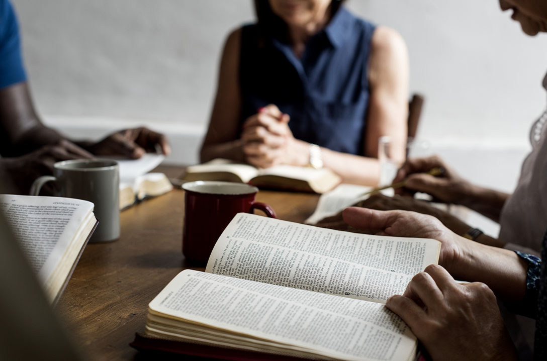 Mulheres em uma mesa com as mãos em cima de uma bíblia aberta cada uma