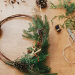 Rustic Christmas wreath. Creative christmas wreath with fir branches, berries, pine cones and herbs with scissors and thread on rural wooden table. Happy holidays. Workshop