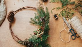 Rustic Christmas wreath. Creative christmas wreath with fir branches, berries, pine cones and herbs with scissors and thread on rural wooden table. Happy holidays. Workshop